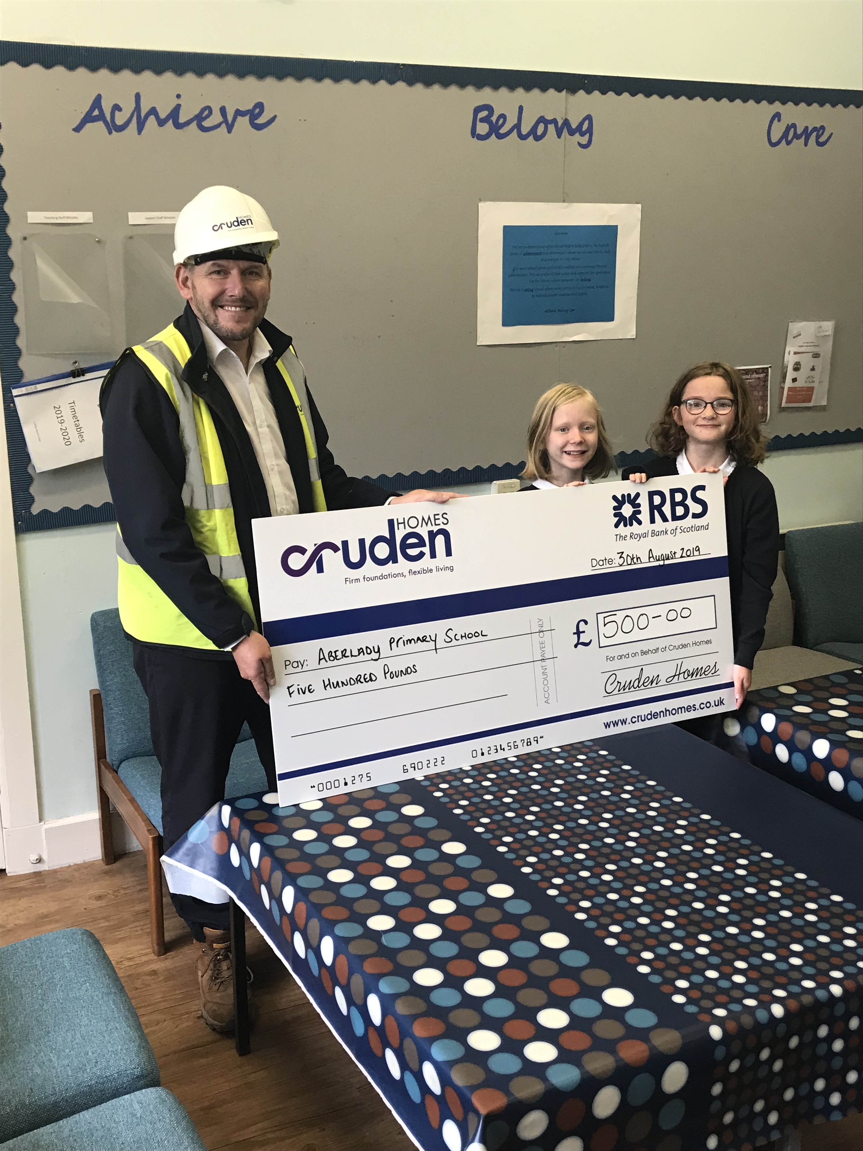 Andy Brown, Contracts Manager for Meadowside, Aberlady, presenting the cheque to two pupils at Aberlady Primary school